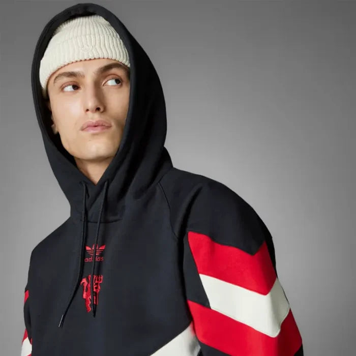 A person wearing a Zing Apparel Manchester United Originals Hoodie with red and white sleeve stripes and a white knit beanie looks off to the side against a plain gray background.